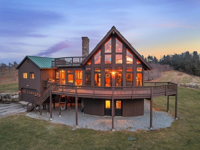 back house at dusk featuring a lawn, a garage, and a wooden deck