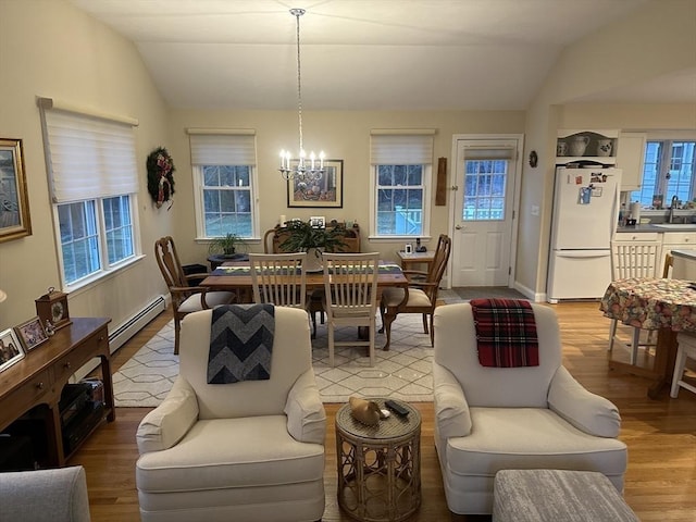 dining space featuring sink, light hardwood / wood-style flooring, an inviting chandelier, a baseboard heating unit, and vaulted ceiling