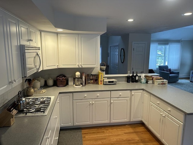 kitchen with white cabinetry, a baseboard radiator, kitchen peninsula, stainless steel gas stovetop, and light hardwood / wood-style floors