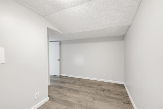 spare room with hardwood / wood-style floors, a textured ceiling, and vaulted ceiling