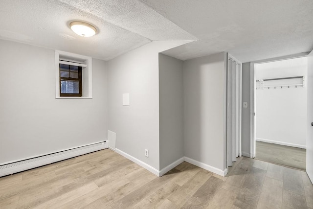 unfurnished room featuring a textured ceiling, light hardwood / wood-style flooring, baseboard heating, and vaulted ceiling