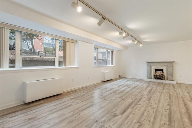 unfurnished living room featuring radiator, a fireplace with raised hearth, baseboards, and wood finished floors