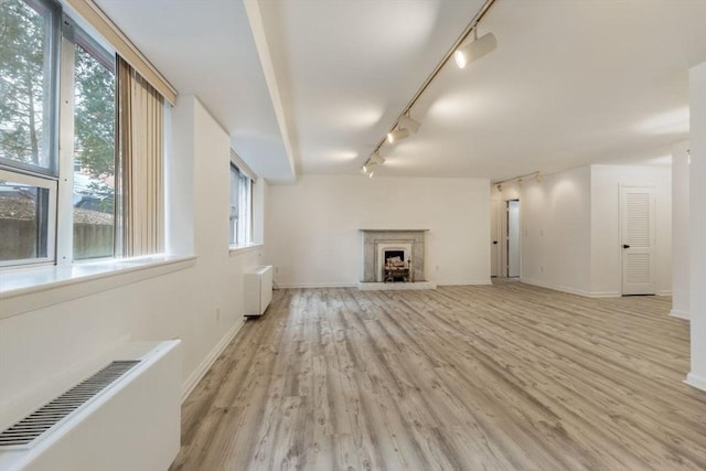 unfurnished living room featuring radiator, a fireplace with raised hearth, visible vents, light wood-style floors, and baseboards