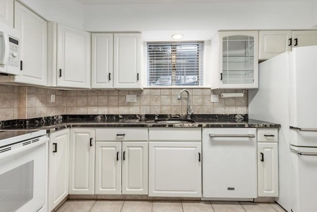 kitchen with backsplash, white cabinetry, a sink, dark stone countertops, and white appliances