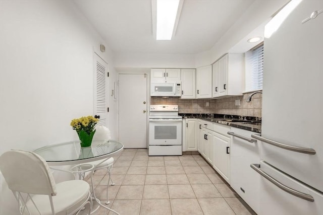 kitchen with dark countertops, backsplash, white cabinetry, a sink, and white appliances