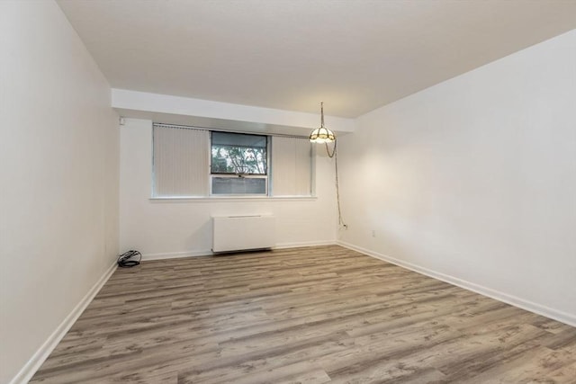 empty room with radiator, wood finished floors, and baseboards