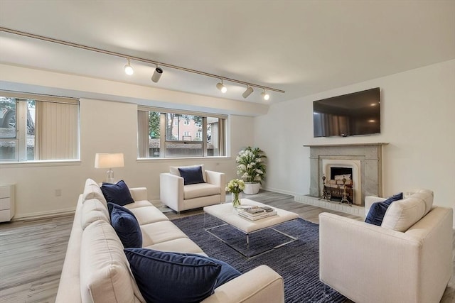 living room with a fireplace with raised hearth, baseboards, and wood finished floors