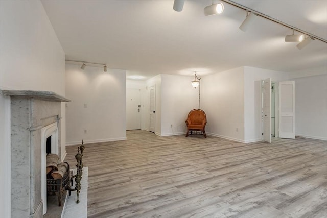 unfurnished room with light wood-style floors, rail lighting, a fireplace with raised hearth, and baseboards