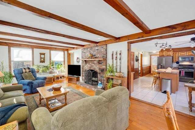 living room featuring a fireplace, light wood-type flooring, beam ceiling, and ceiling fan