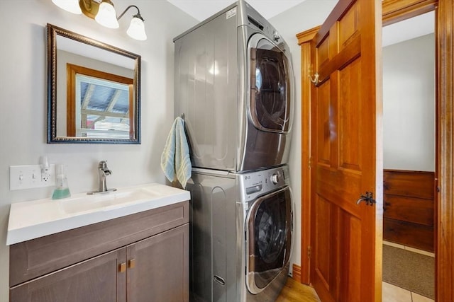 laundry area with sink, stacked washer / drying machine, and cabinets