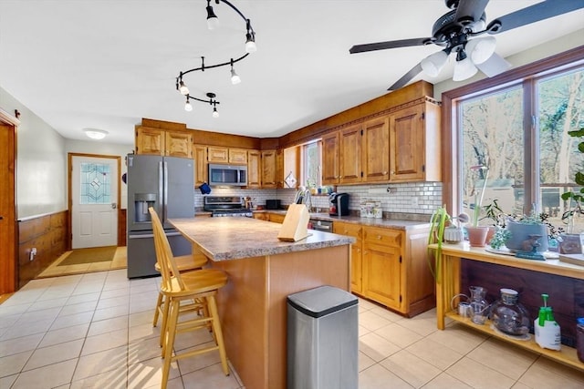 kitchen with stainless steel appliances, tasteful backsplash, light tile patterned floors, a breakfast bar area, and a kitchen island