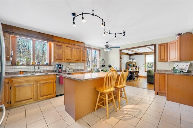 kitchen featuring sink, a center island, ceiling fan, stainless steel dishwasher, and a breakfast bar