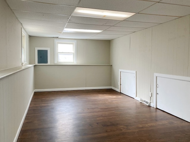 empty room with wooden walls, electric panel, a drop ceiling, and dark wood-type flooring