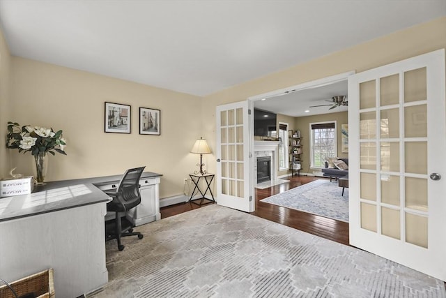 office area featuring french doors, wood finished floors, a ceiling fan, a fireplace, and baseboards