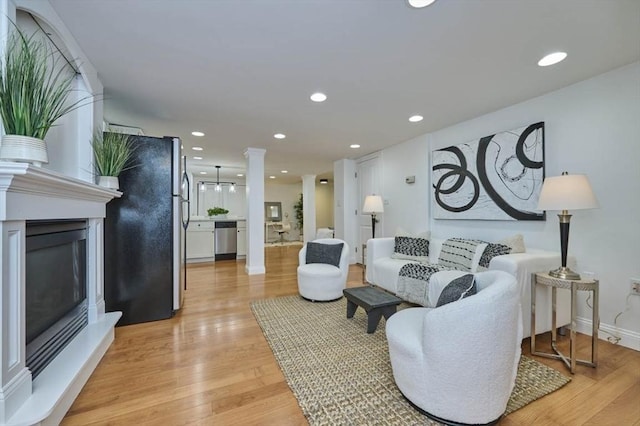 living room featuring ornate columns, baseboards, recessed lighting, and light wood-style floors