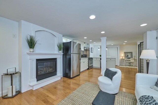 living room featuring ornate columns, a glass covered fireplace, recessed lighting, and light wood-type flooring