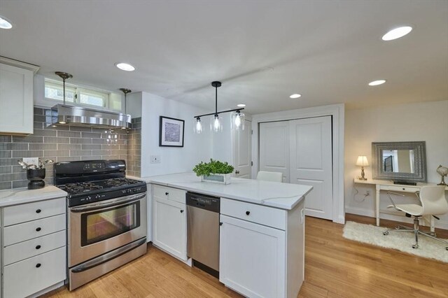kitchen with a peninsula, wall chimney exhaust hood, white cabinets, light wood-style flooring, and appliances with stainless steel finishes
