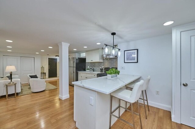 kitchen with decorative columns, light wood-type flooring, freestanding refrigerator, a breakfast bar, and gas range oven