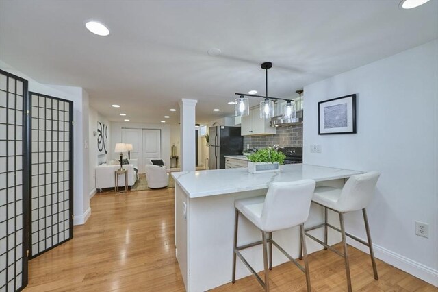 kitchen with baseboards, freestanding refrigerator, a peninsula, and white cabinets