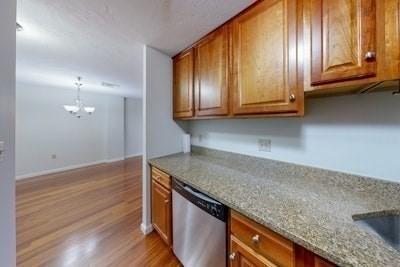 kitchen featuring dishwasher, an inviting chandelier, hanging light fixtures, light stone countertops, and light wood-type flooring