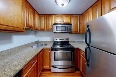 kitchen with light stone counters, sink, stainless steel appliances, and light wood-type flooring