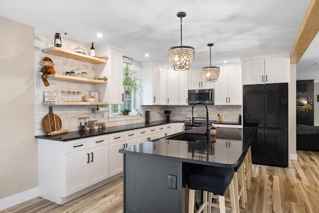 kitchen with black refrigerator, light wood-style flooring, stainless steel microwave, dark countertops, and a notable chandelier