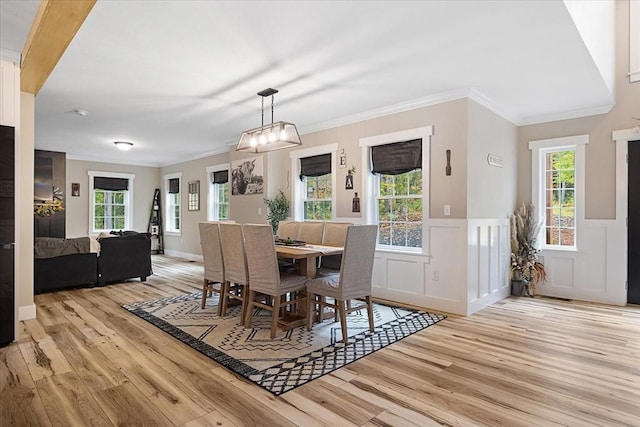dining space featuring light wood-style floors, a decorative wall, ornamental molding, and a wainscoted wall