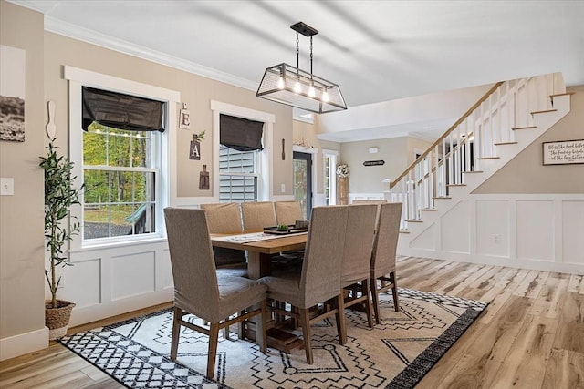 dining space featuring a decorative wall, stairway, light wood-type flooring, and ornamental molding