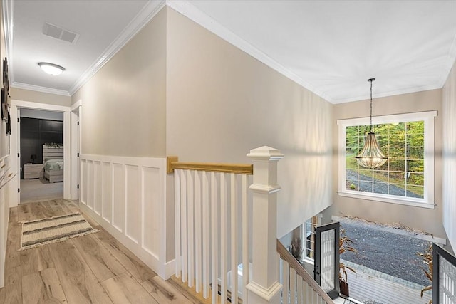 hall with crown molding, visible vents, a wainscoted wall, wood finished floors, and an upstairs landing