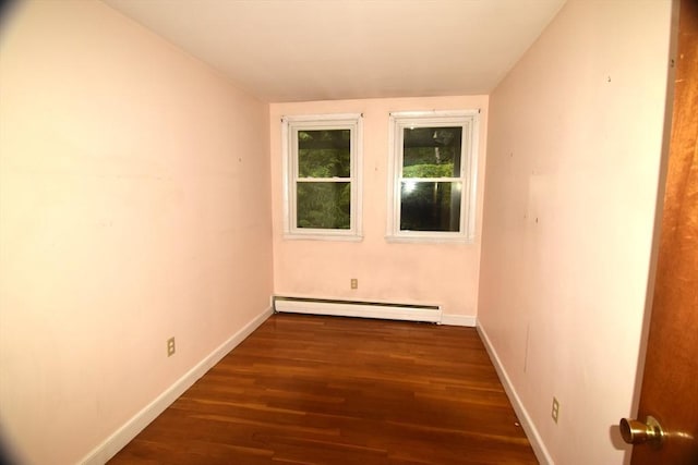 spare room featuring a baseboard heating unit, dark wood-style flooring, and baseboards