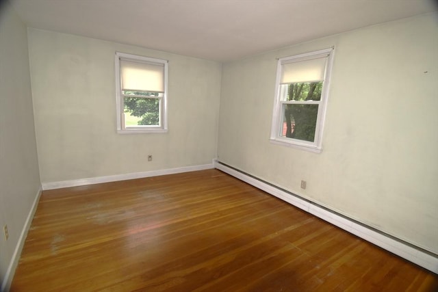 unfurnished room with a baseboard heating unit, healthy amount of natural light, and wood finished floors