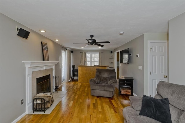 living room with ceiling fan, a tiled fireplace, and light hardwood / wood-style floors