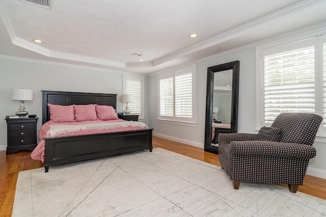 bedroom featuring a raised ceiling, multiple windows, and light wood-type flooring