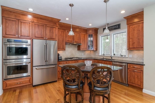 kitchen with stainless steel appliances, sink, decorative light fixtures, a center island, and light wood-type flooring