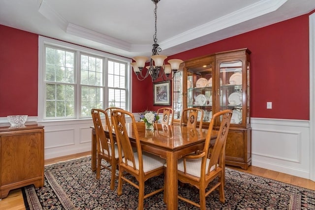 dining area with a raised ceiling, crown molding, a notable chandelier, and light hardwood / wood-style flooring