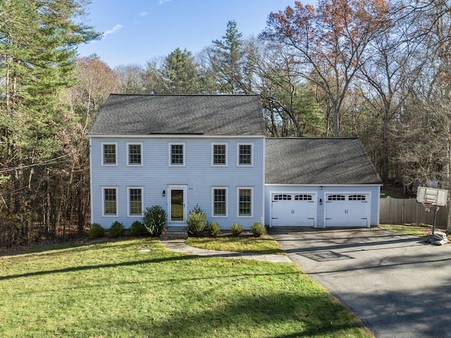 colonial house featuring aphalt driveway, a shingled roof, an attached garage, a front yard, and fence