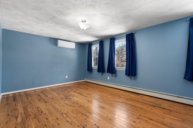 unfurnished room featuring baseboards, wood-type flooring, a textured ceiling, an AC wall unit, and a baseboard heating unit