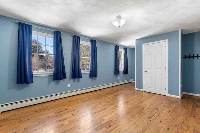 empty room with a baseboard radiator, a textured ceiling, baseboards, and hardwood / wood-style floors