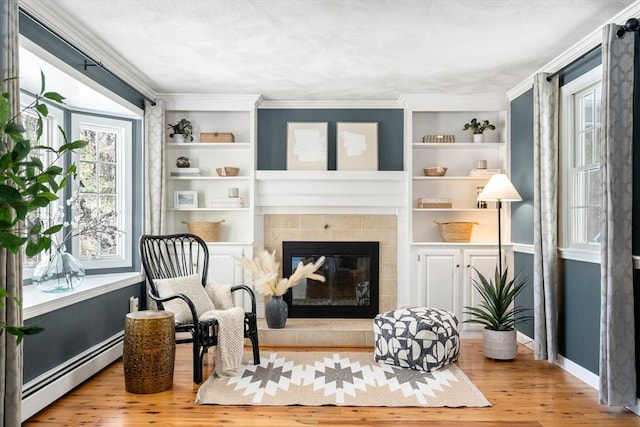 living area featuring a baseboard heating unit, a tiled fireplace, wood finished floors, and built in features