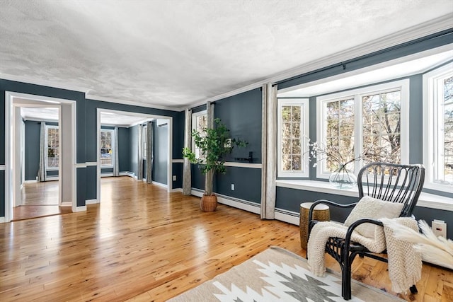 living area with baseboards, a baseboard heating unit, light wood-type flooring, and crown molding