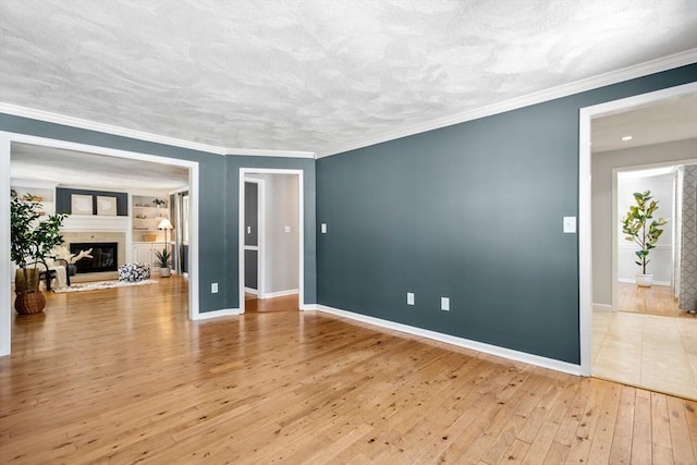 empty room featuring a fireplace with raised hearth, hardwood / wood-style floors, ornamental molding, and baseboards