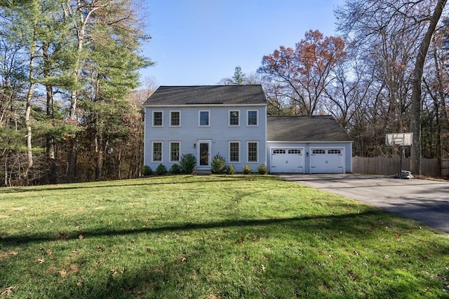 colonial inspired home with a garage, aphalt driveway, a front lawn, and fence