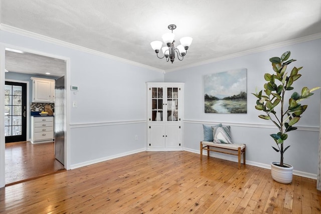 unfurnished room with light wood finished floors, baseboards, ornamental molding, and a chandelier