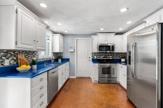 kitchen featuring tasteful backsplash, white cabinets, dark countertops, appliances with stainless steel finishes, and a sink