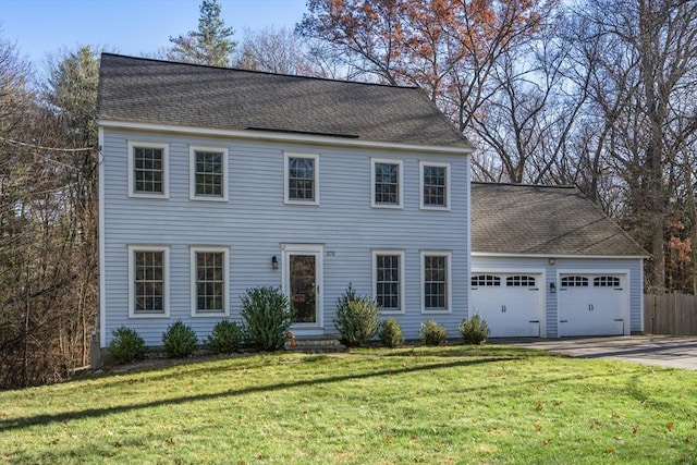 colonial house featuring an attached garage, driveway, a front lawn, and roof with shingles