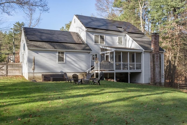 rear view of house with a chimney, a sunroom, a lawn, and a fire pit