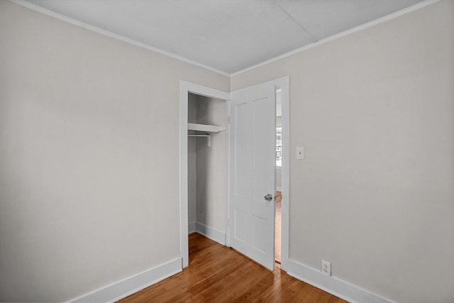 unfurnished bedroom featuring crown molding, a closet, wood finished floors, and baseboards