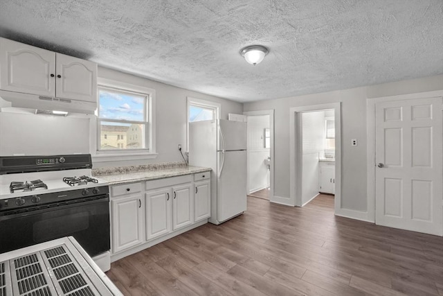 kitchen with light wood-type flooring, under cabinet range hood, freestanding refrigerator, and range with gas cooktop