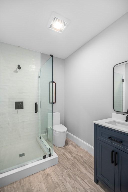 bathroom with wood-type flooring, toilet, a shower with shower door, and vanity