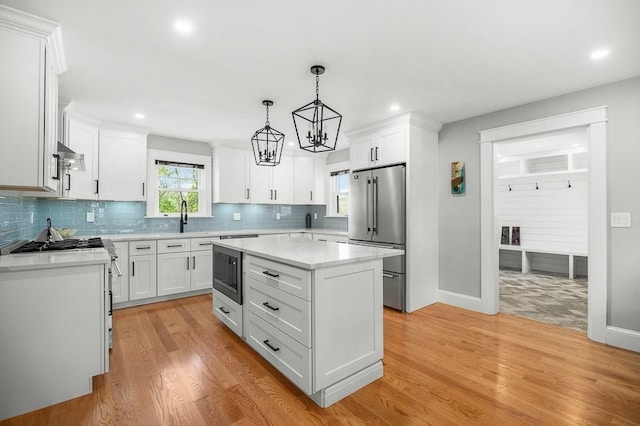 kitchen with appliances with stainless steel finishes, pendant lighting, white cabinetry, a center island, and light hardwood / wood-style floors